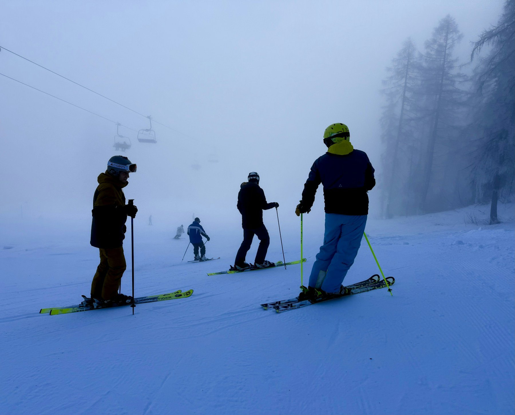 Skiers beside a chairlift on a foggy slope