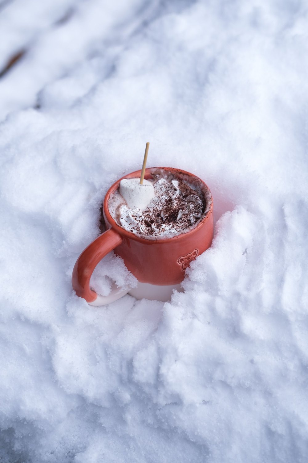 A red mug of hot chocolate resting in the snow